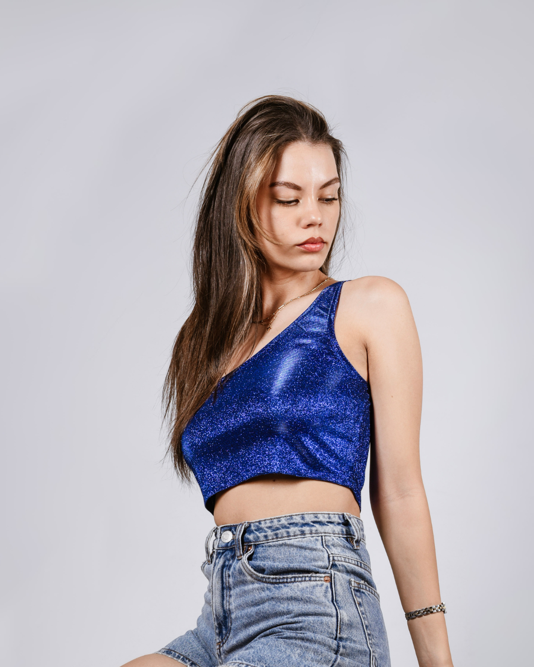 Woman wearing a blue sparkly top and jeans against a plain background