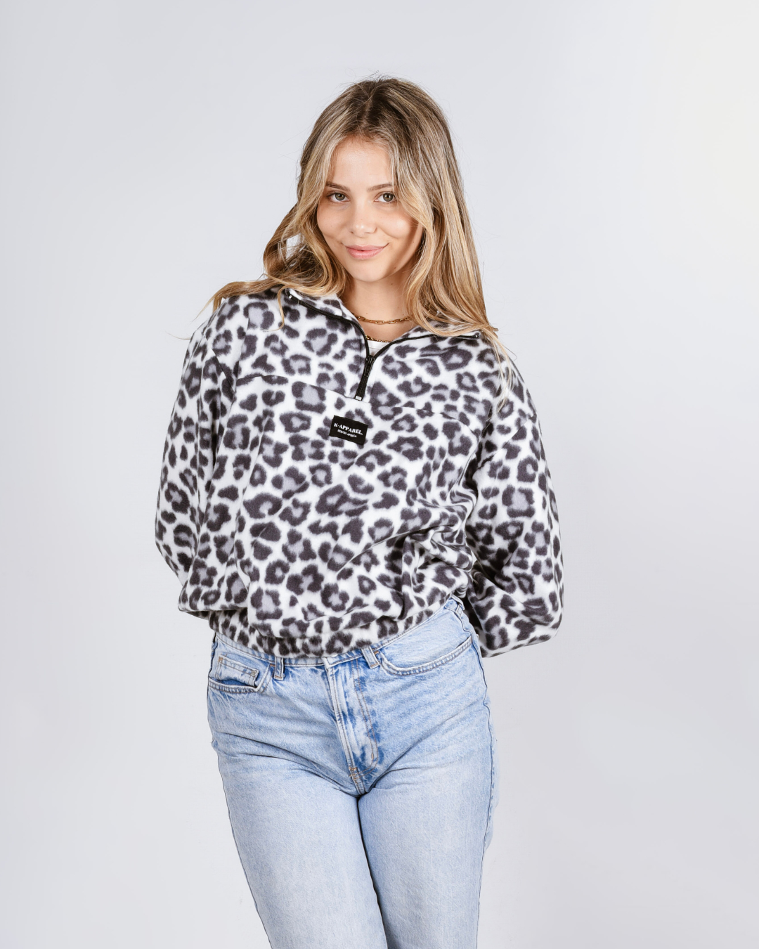 Woman wearing a leopard print sweatshirt and light blue jeans on a plain background