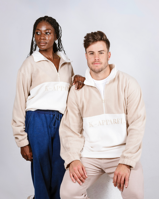 Two people wearing matching beige and white retro quarter zip fleece jerseys with visible branding on a plain background.