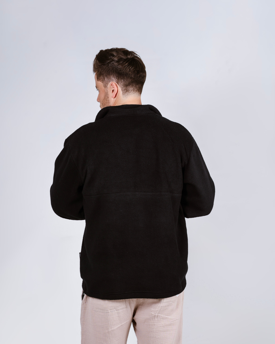 Man wearing a black quarter zip fleece pullover with a brand logo on a light gray background