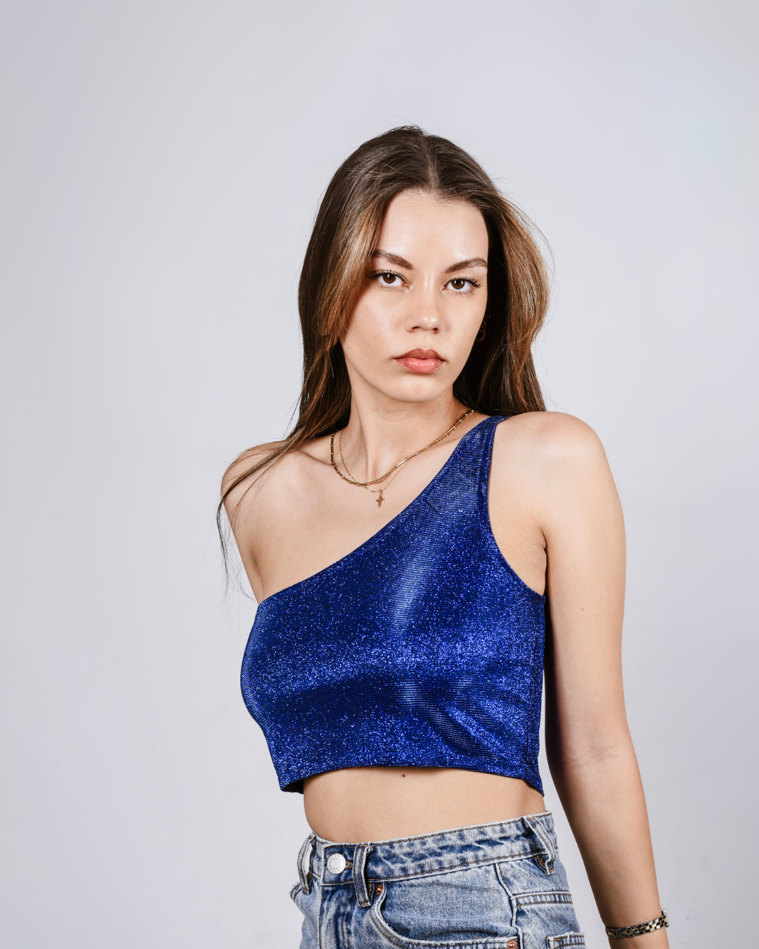 Woman wearing a blue sparkly top and jeans against a plain background