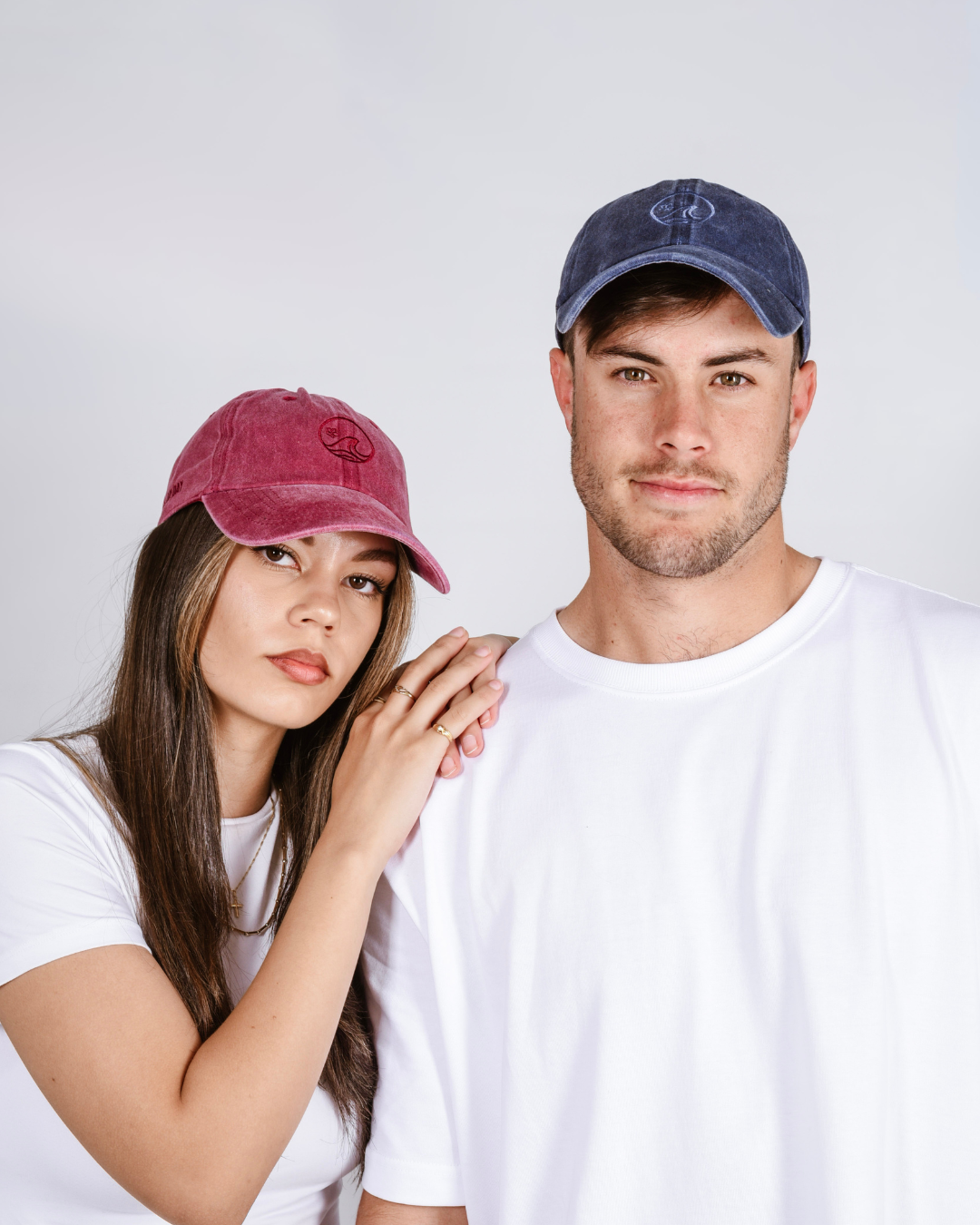 Two people wearing baseball caps against a plain background