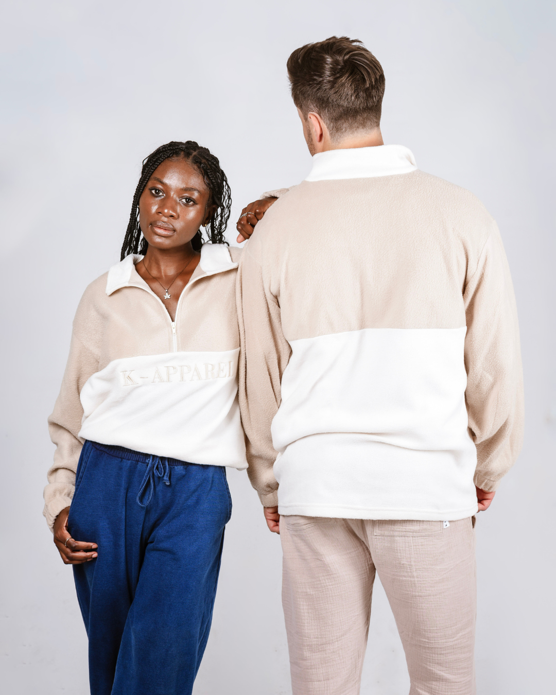 Two people wearing matching beige and white quarter zip fleece jerseys with visible branding on a plain background.