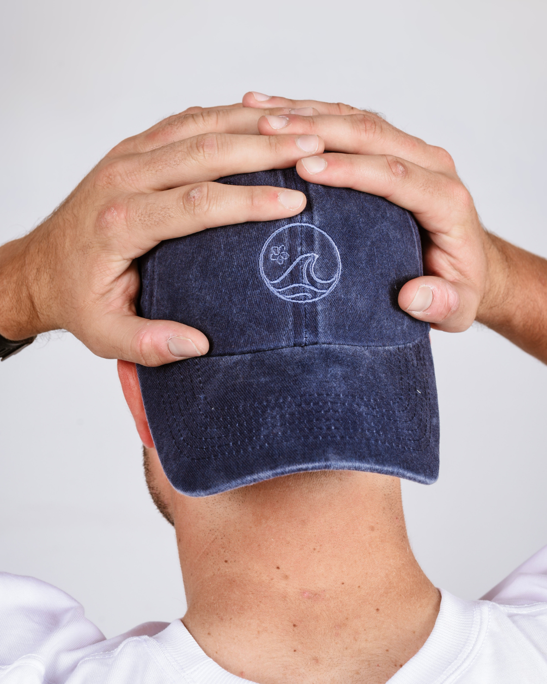 Navy blue cap with a logo held by hands against a white background