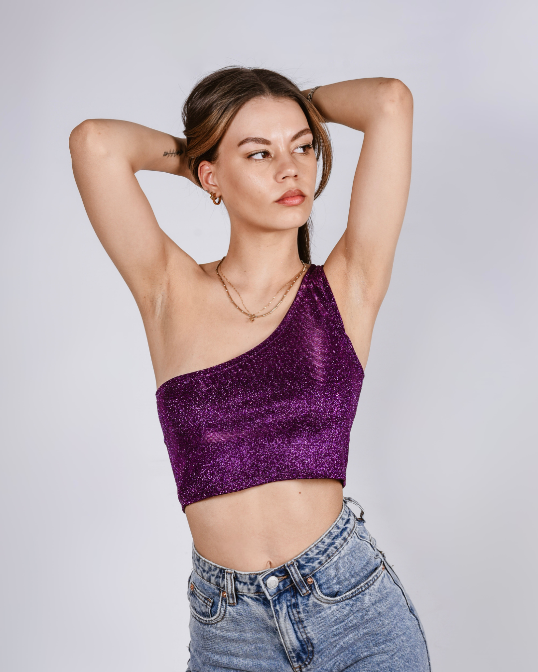 Woman wearing a purple glittery top and denim shorts against a light gray background