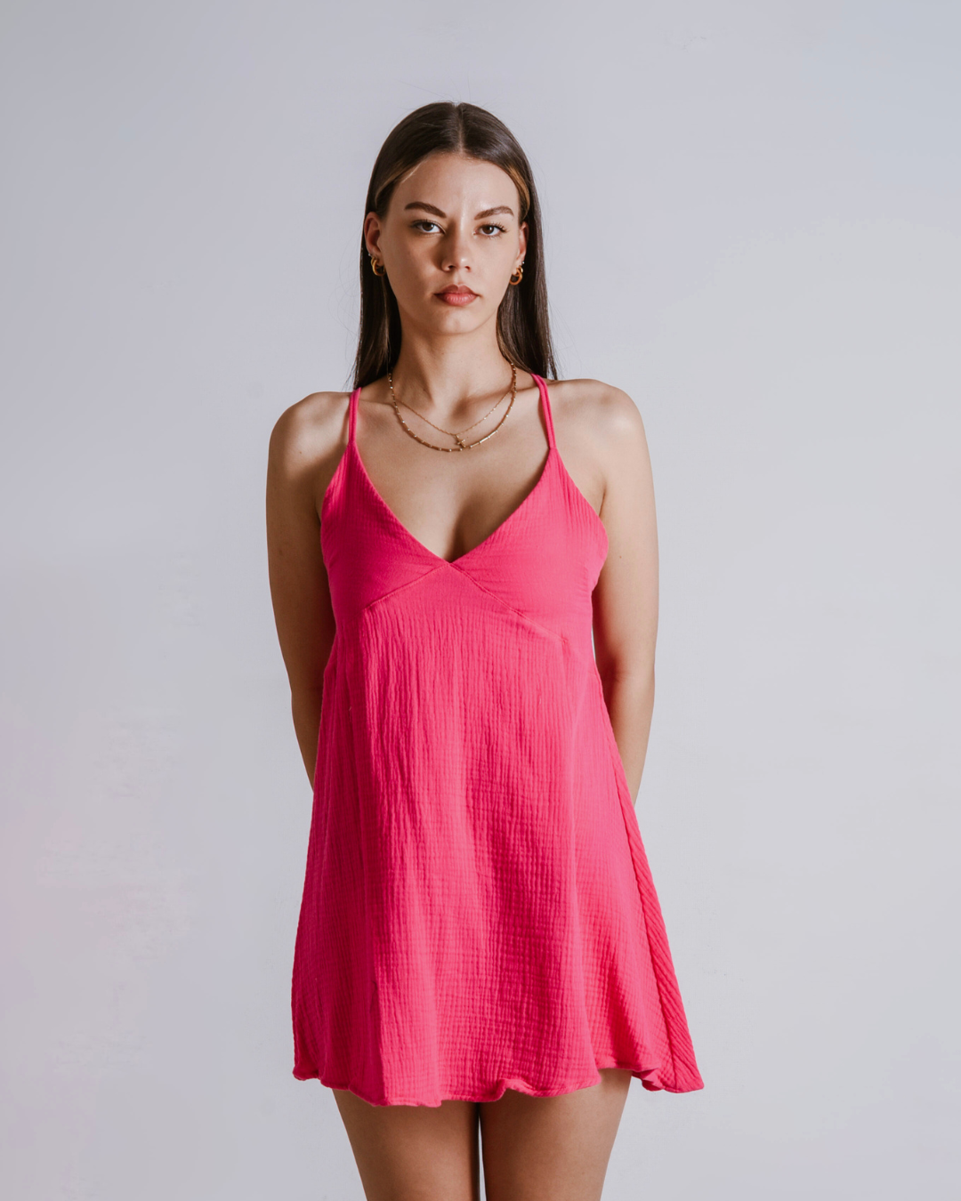 Woman wearing a shocking pink cotton dress against a plain background
