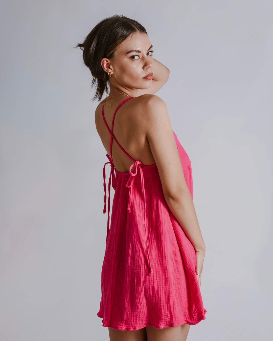 Woman wearing a shocking pink cotton dress against a plain background