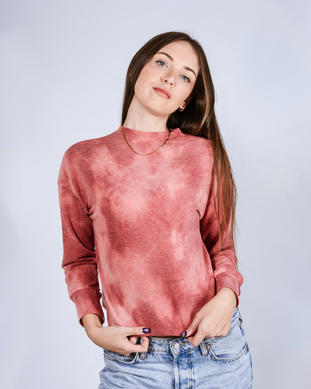 Woman wearing a pink- red tie dye crop top against a light gray background