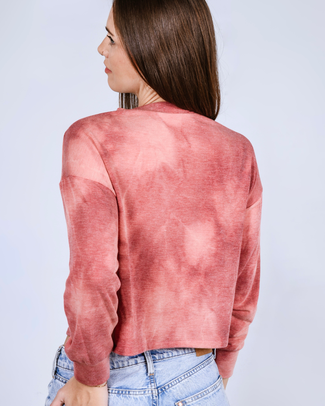 Woman wearing a pink- red tie dye crop top against a light gray background