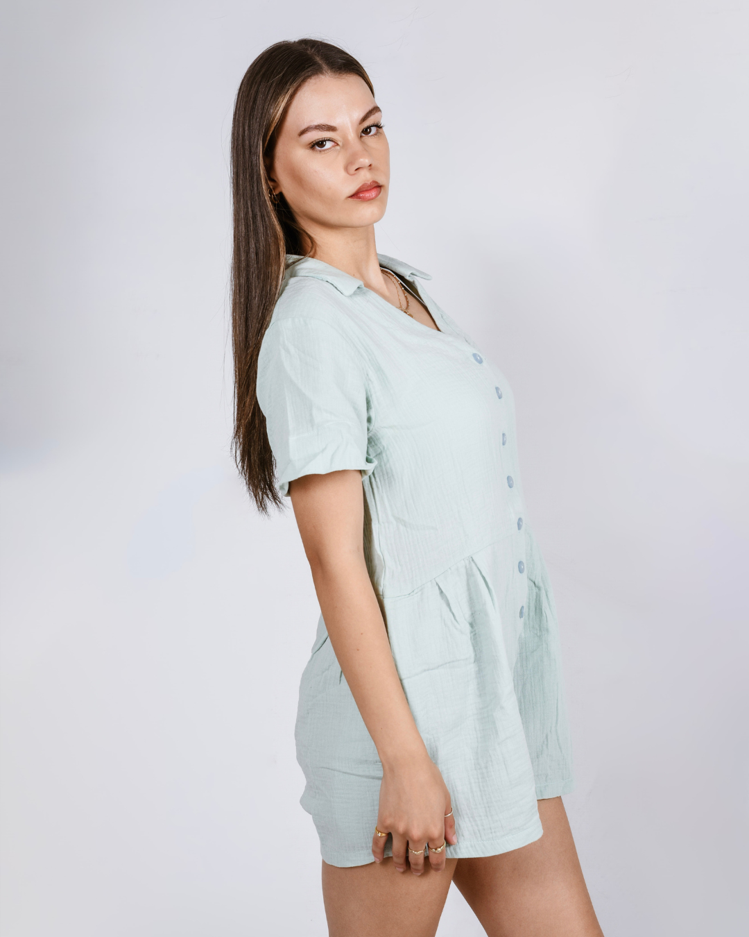 Woman wearing a sage button up romper with pockets, against a white background