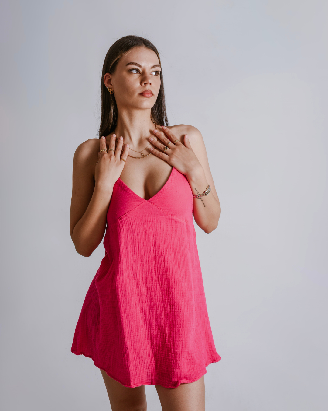 Woman wearing a shocking pink cotton dress against a plain background