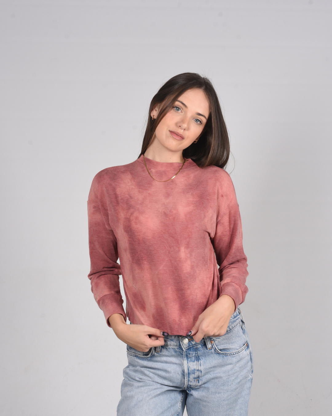 Woman wearing a pink- red tie dye crop top against a light gray background
