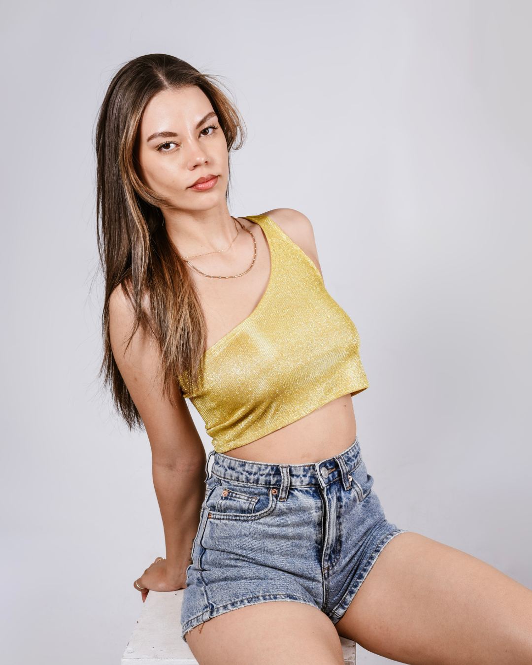 Woman wearing a yellow glitter top and denim shorts posing against a plain background