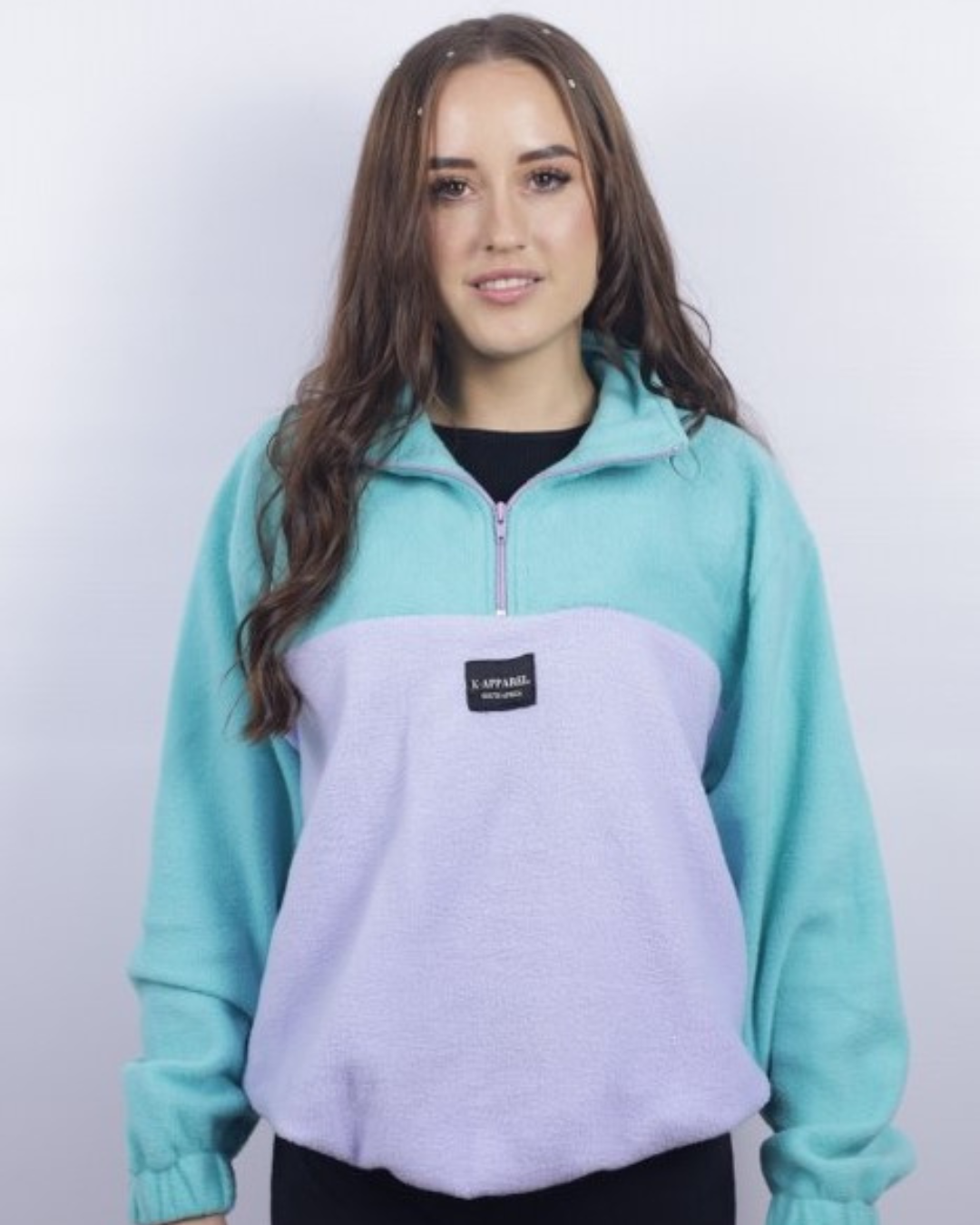 A woman wearing a color-blocked quarter-zip fleece pullover with a mint green upper section and sleeves, and a light lavender lower section, featuring a small black 'S. PUBLISHER' brand patch on the chest.