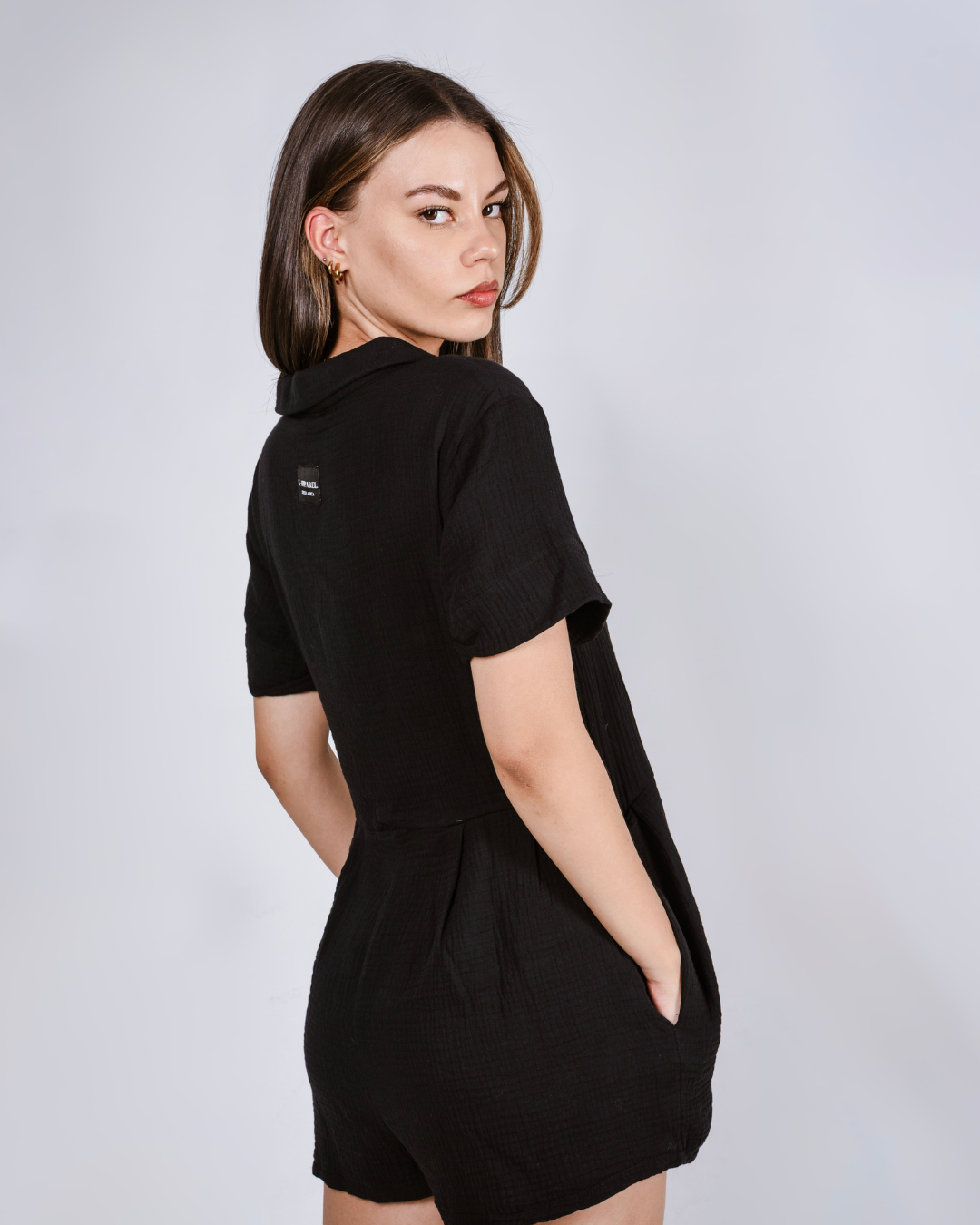 Woman wearing a black button up cotton romper with pockets. Side view