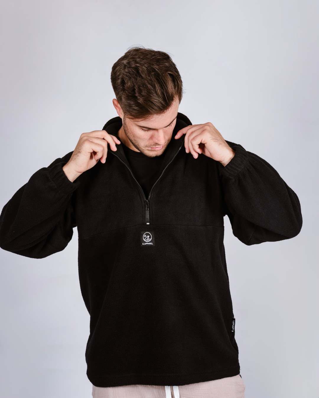 Man wearing a black quarter zip fleece pullover with a brand logo on a light gray background