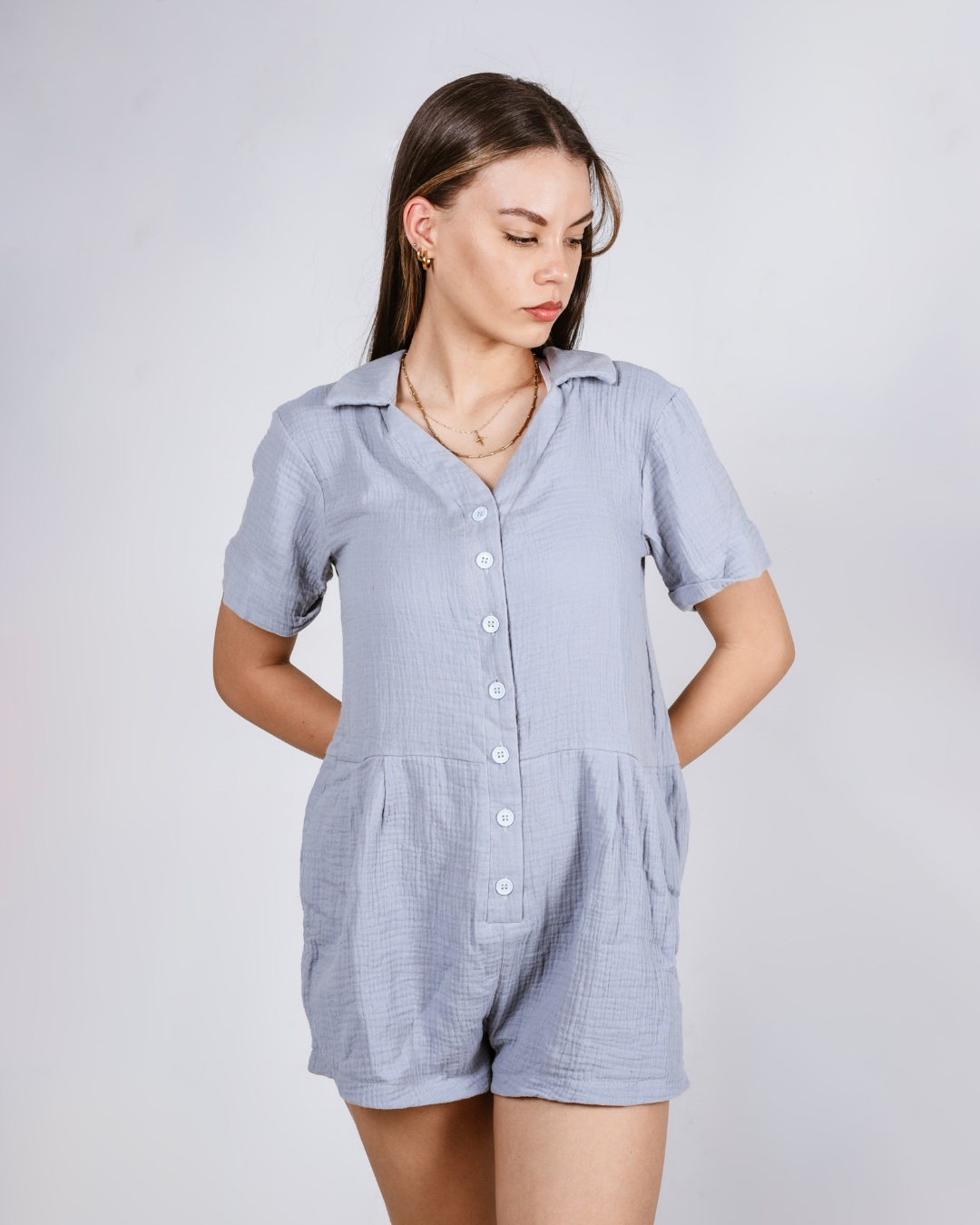 Woman wearing a blue button up cotton romper with pockets, against a white background