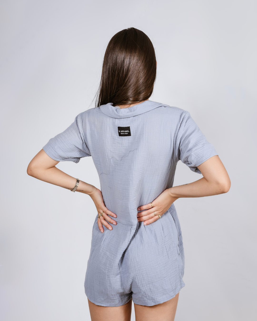 Woman wearing a blue button up cotton romper with pockets, against a white background