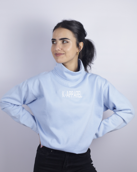 Woman wearing a light blue turtleneck sweater with 'K. APPAREL' branding on a plain background