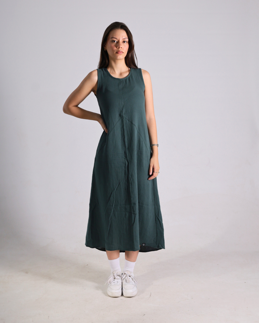 A woman modeling a sleeveless, dark green midi dress with white sneakers against a plain light gray studio background.