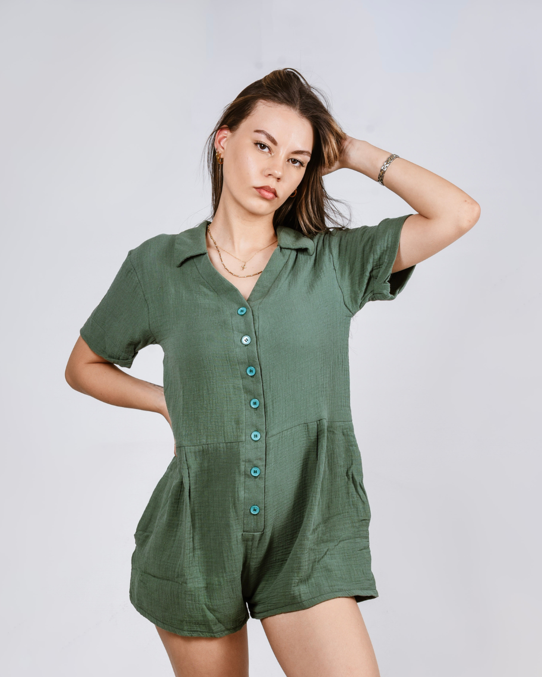 Woman wearing a green button up cotton romper with pockets, against a white background
