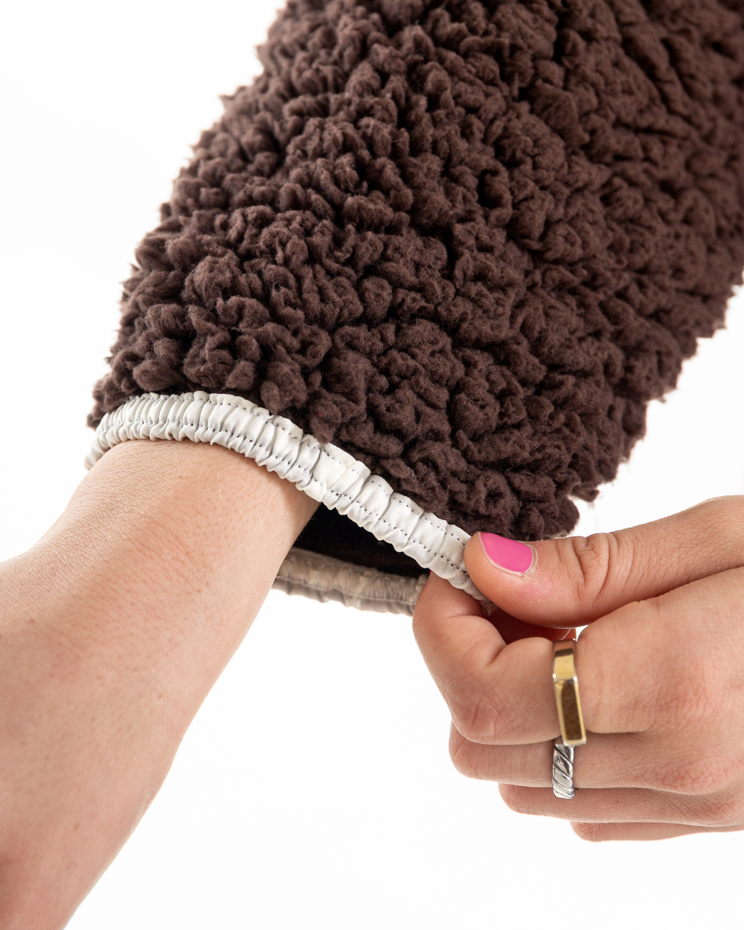 A close-up of a person's hands demonstrating the stretchiness of a brown sherpa fleece sleeve, with one hand pulling the elasticated cuff outward against a white background.