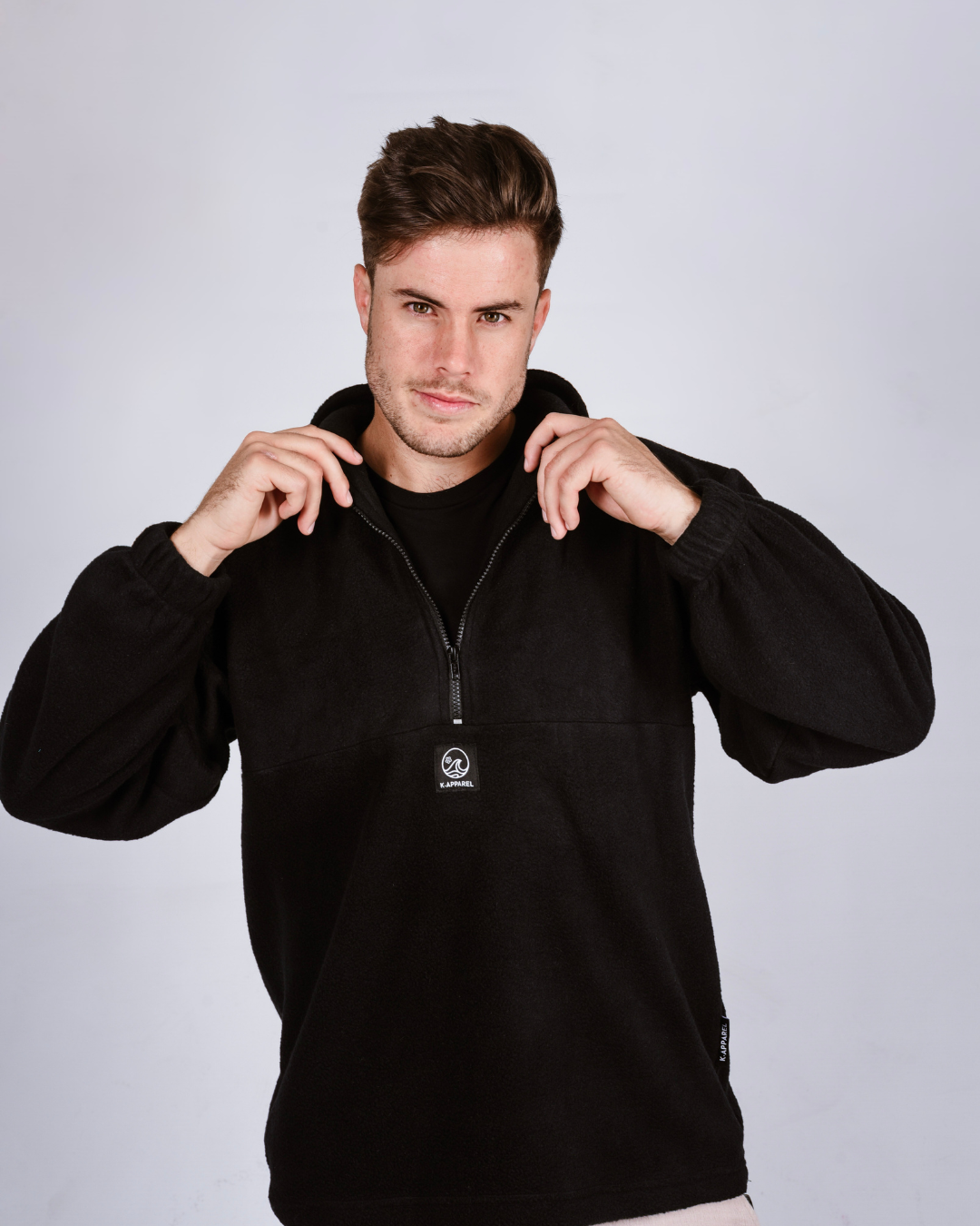 Man wearing a black quarter zip fleece pullover with a brand logo on a light gray background
