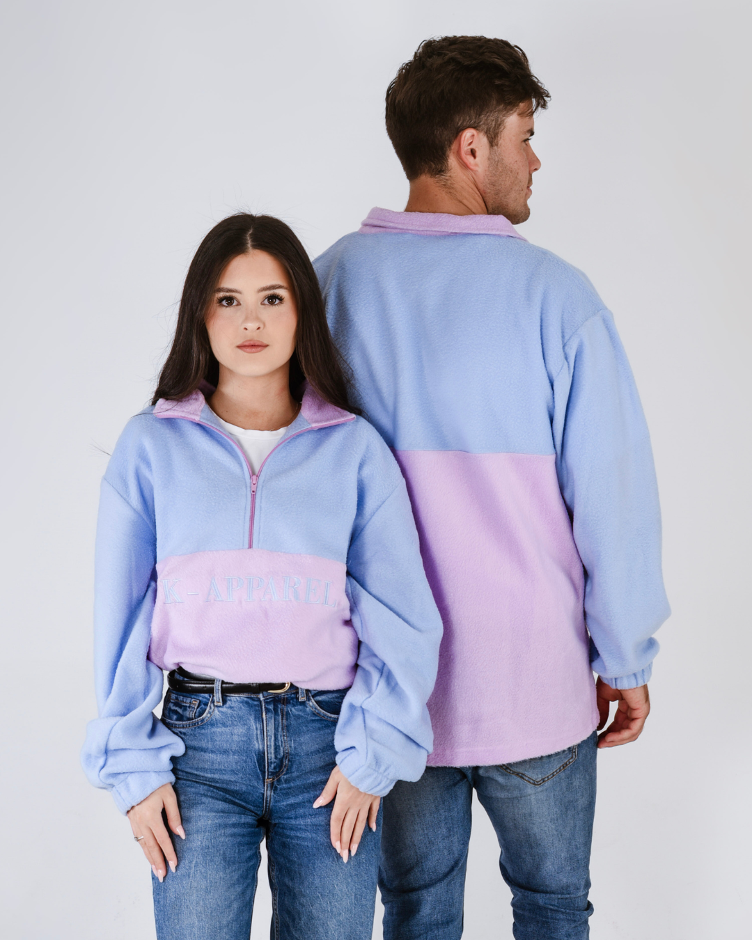 Two people wearing matching pink and blue retro quarter zip fleece jerseys with visible branding on a plain background.