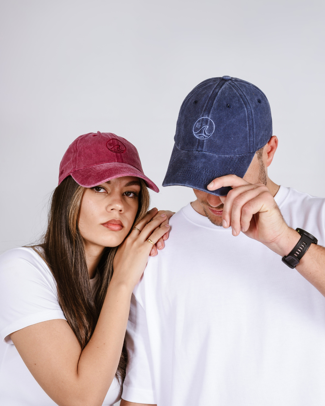 Two people wearing baseball caps against a plain background- red and blue caps 