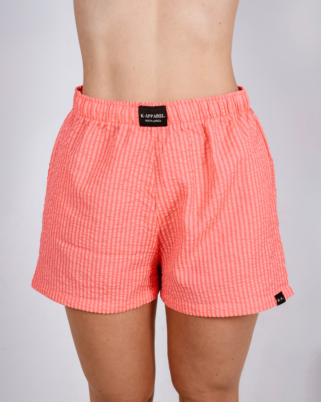 Person wearing coral  checkered high waisted shorts and a white top on a plain background
