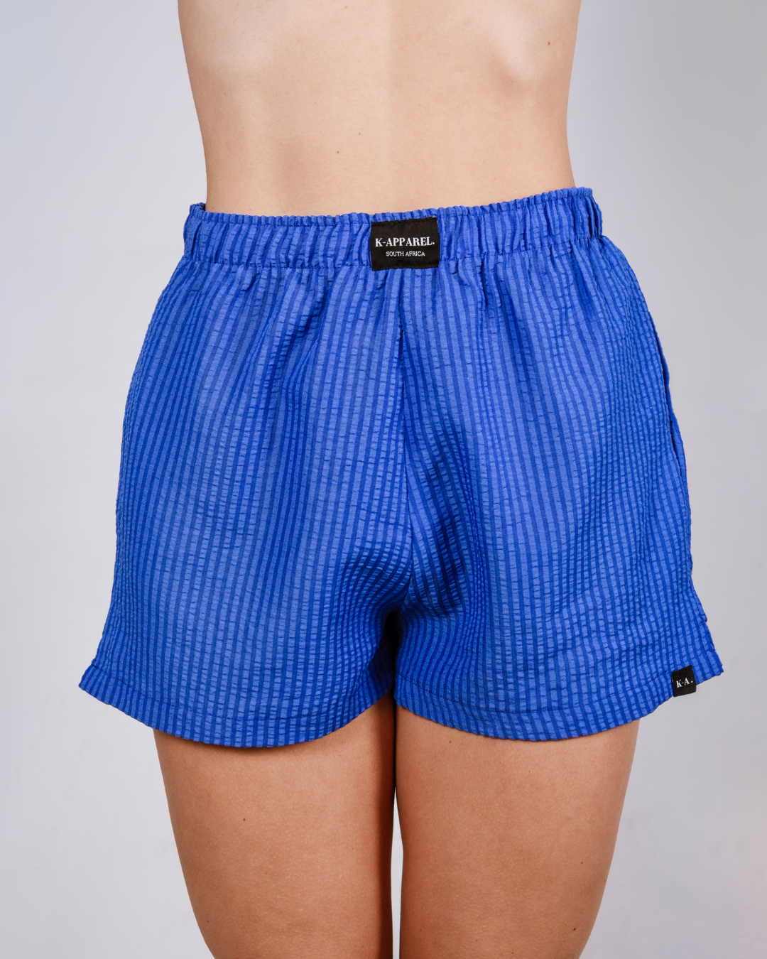 Person wearing navy checkered high waisted shorts and a white top on a plain background
