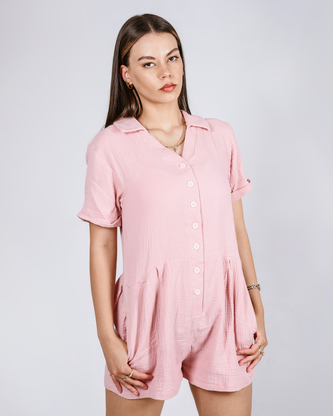 Woman wearing a pink button up cotton romper with pockets, against a white background