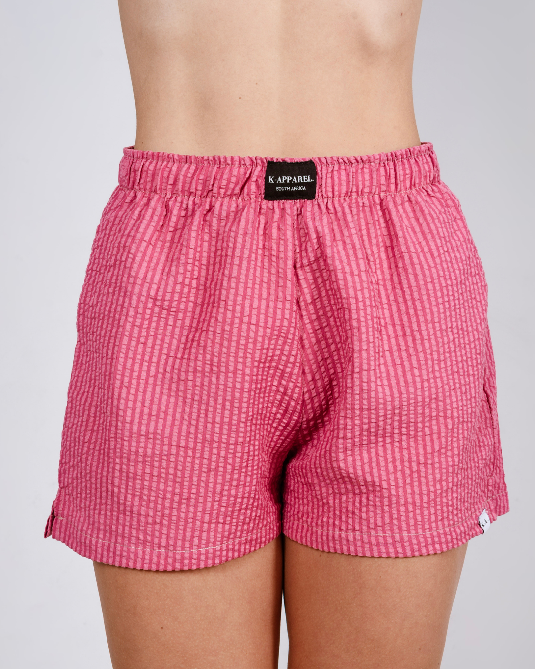 Person wearing pink checkered high waisted shorts and a white top on a plain background
