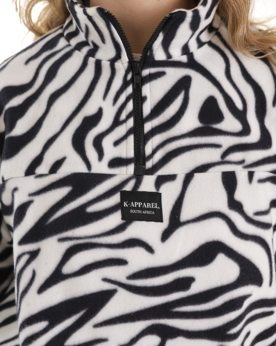Close-up of a person wearing a black and white zebra-patterned fleece pullover with a black zipper and a visible K-APPAREL brand patch on the chest.